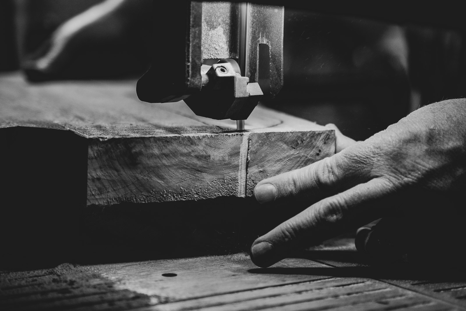 Main d'artisan guidant une pièce de bois sur la machine, à l'atelier